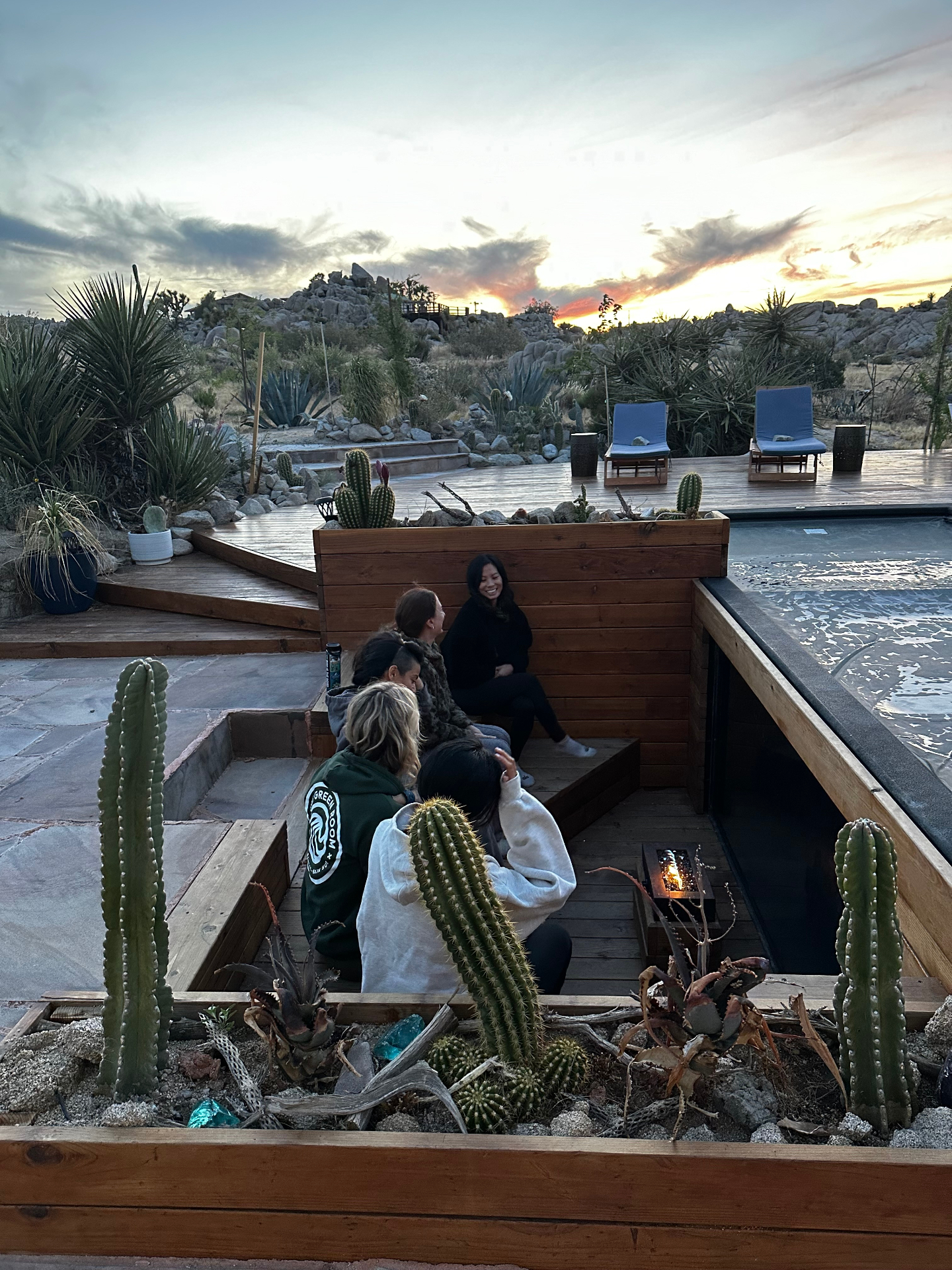 Guests gathered around a sunset firepit beside a hot tub